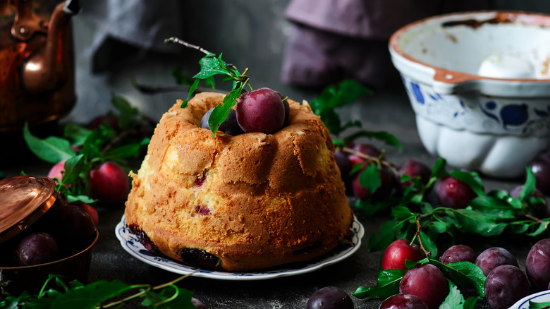A plum sour cream cake garnished with plums and presented with plums and a bowl of sour cream on the side