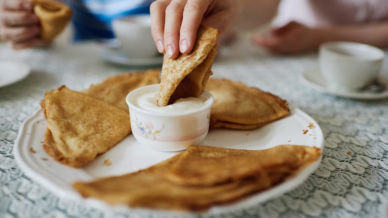 Hand dipping blini into a ramekin of sour cream