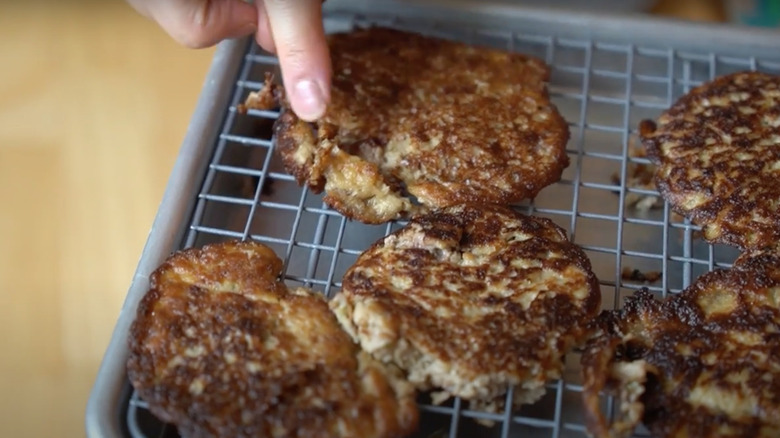Finger pointing to sour cream and beef burger patties on a wire rack