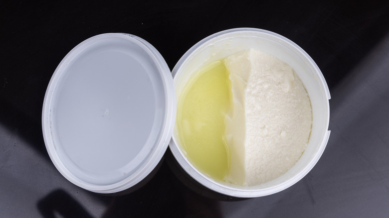 Overhead image of a sour cream container with the liquid whey separated from the cream