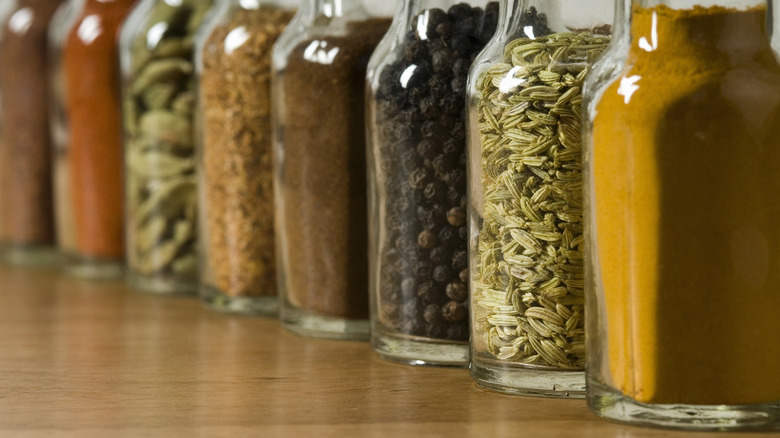 Various seasonings lined up in glass jars on wood surface