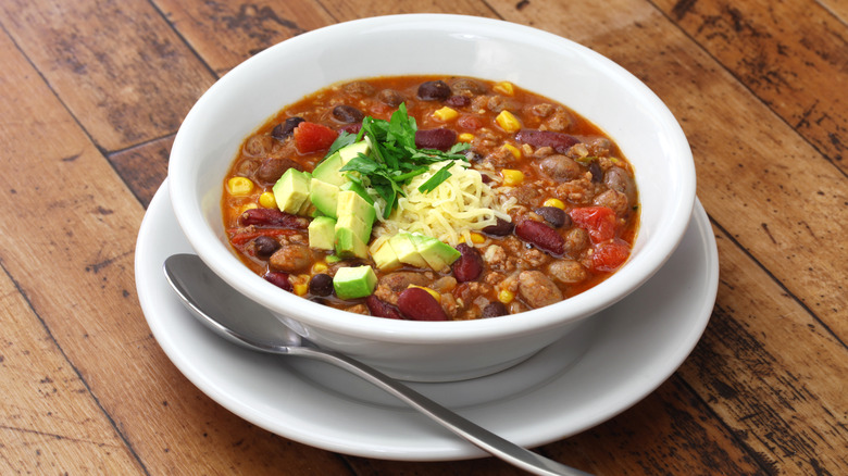 Bowl of taco soup topped with cheese, cilantro, and avocado on a wood surface