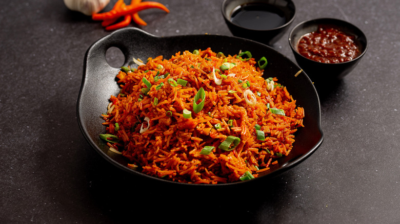 Flavored rice in a black bowl besides sauces on a dark surface