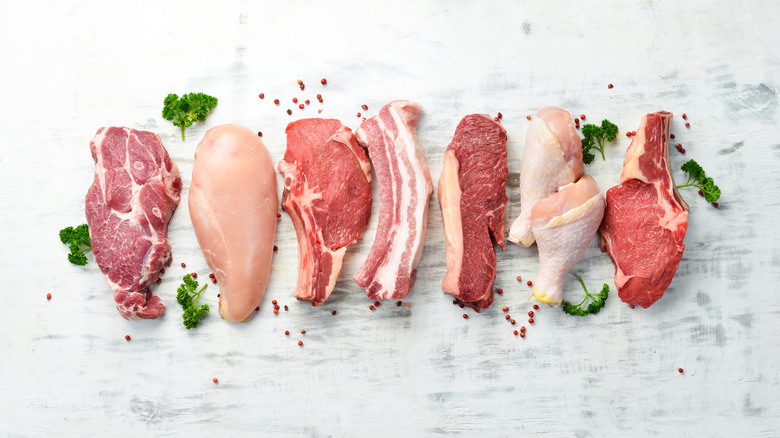 Different cuts of chicken, beef, and pork lined up on a white background