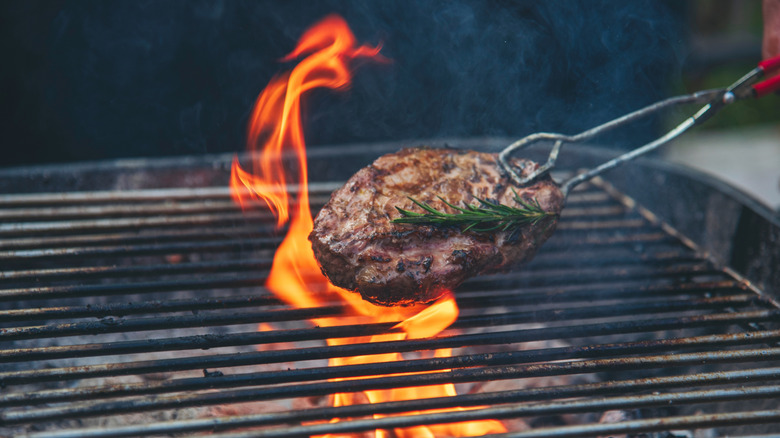 A burger being flipped on a grill with flames