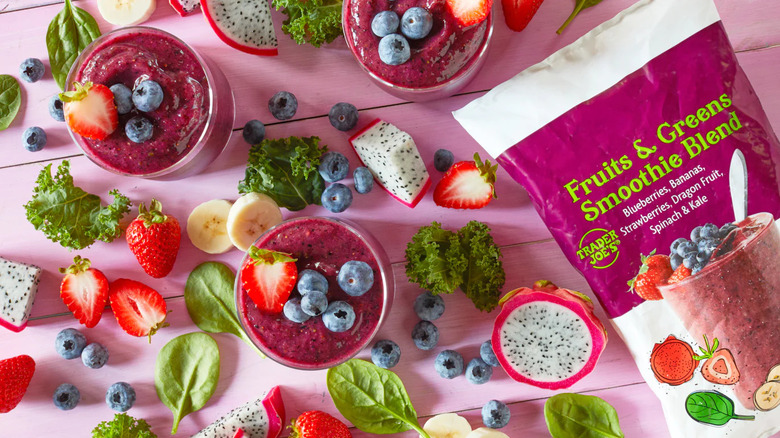 bag of trader joe's smoothie blend, scattered fruits and vegetables, and 3 smoothies against a pink background