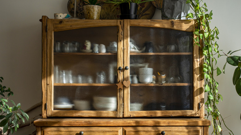 A close-up of a wood china cabinet with dishes behind glass doors