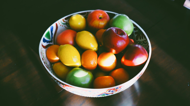 Sun shining on a bowl of fake fruit on a dark table