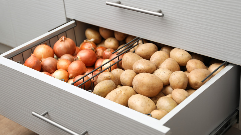 A kitchen drawer pulled out to display piles of potatoes and onions