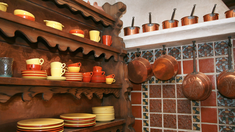 An old-fashioned kitchen with dishes on open shelves and copper pots hanging from hooks