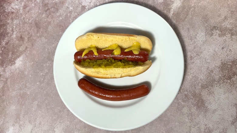 Well-browned and slightly curved broiled hot dogs, plain and in a bun with relish and mustard.