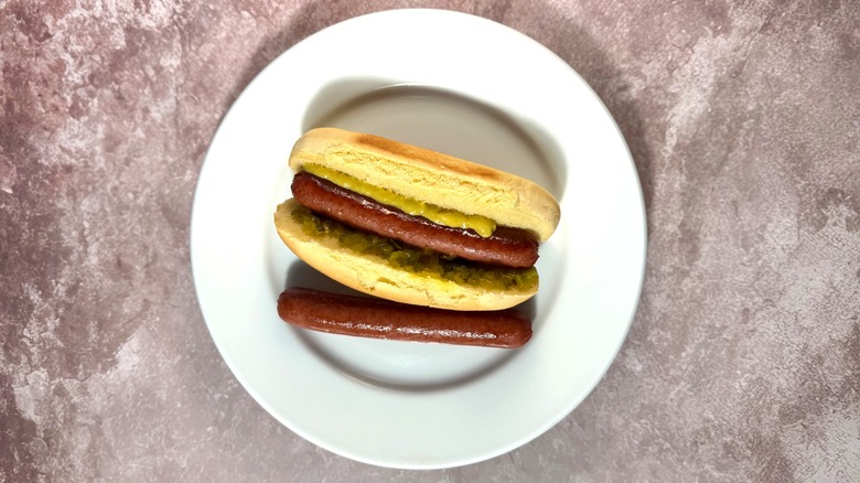Glossy brown pan-seared hot dogs, plain and in a bun with relish and mustard.