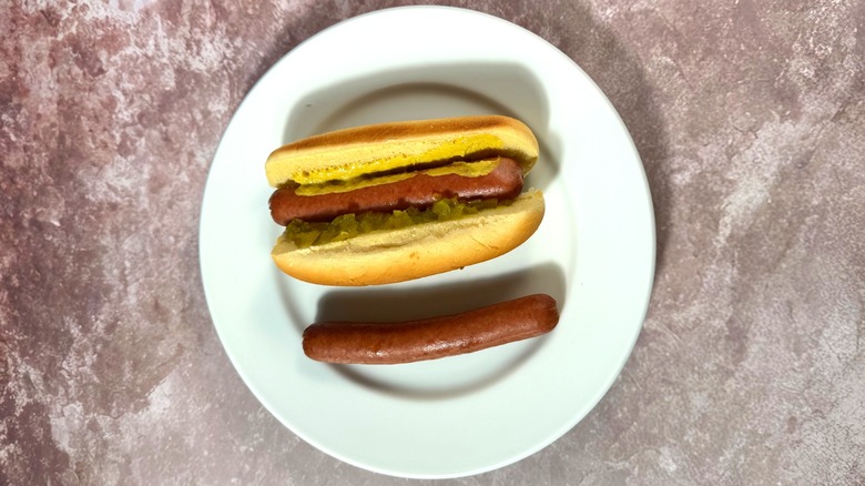 Light brown simmered hot dogs, plain and in a bun with relish and mustard.