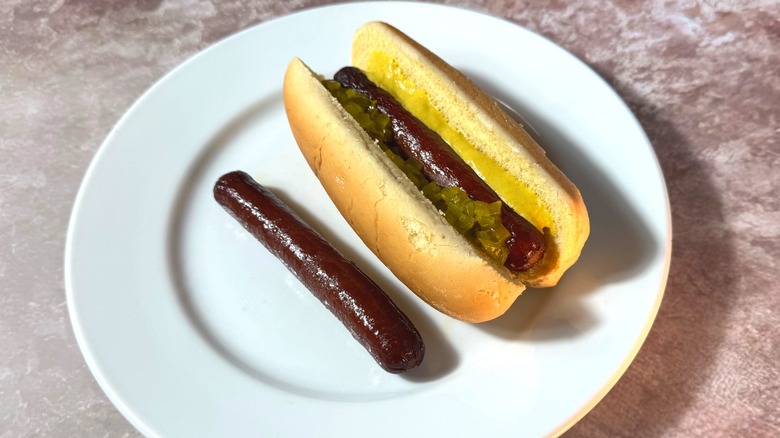 Dark brown slow-cooked hot dogs, plain and in a bun with relish and mustard.