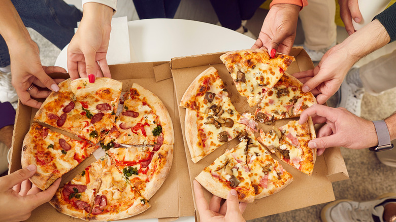 A close up of a group of people pulling pieces of pizza from two boxes