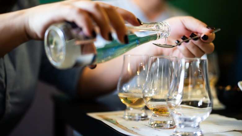 Close up of a bartender using a measured spoon to add water to glasses of whiskey