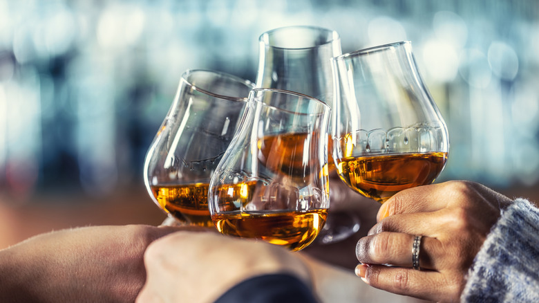 A closeup of four people cheersing whiskey glasses