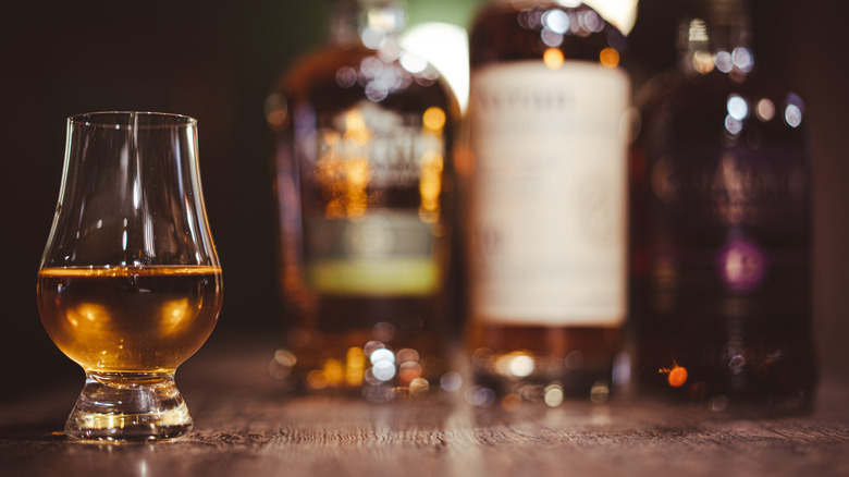Closeup of a glass of whiskey in front of three bottles