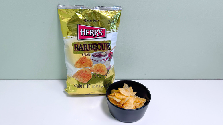 A bowl of chips next to a bag of Herr's Barbecue Chips
