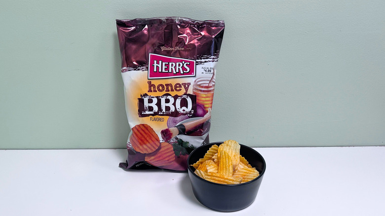 A bowl of chips next to a bag of Herr's Honey BBQ Chips