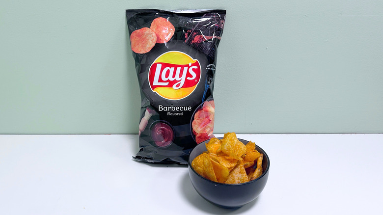 A bowl of chips next to a bag of Lay's Barbecue Chips