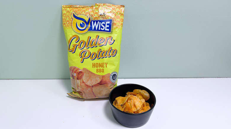 A bowl of chips next to a bag of Wise Golden Potato Honey BBQ Chips