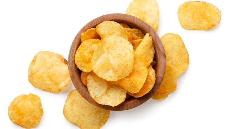 Overflowing potato chips in a wooden bowl on a white background