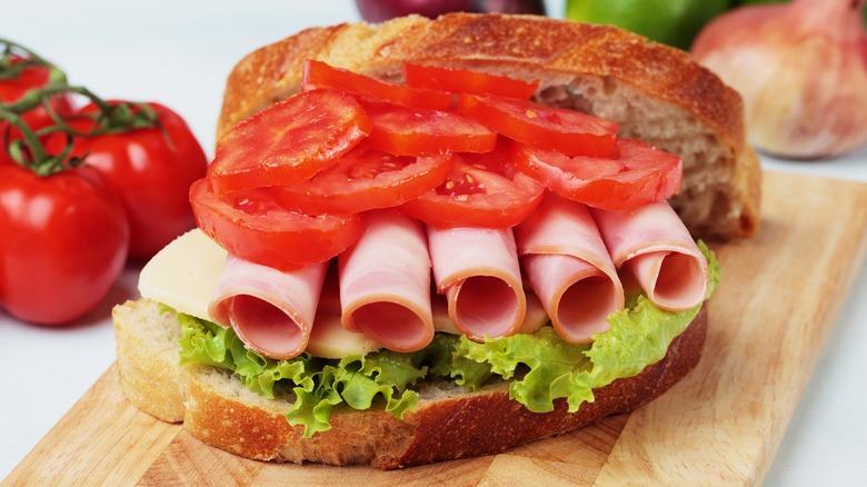 Bologna sandwich with lettuce, tomato, and cheese on a cutting board