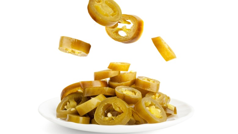 A plate of pickled jalapeños with more falling onto the plate on a white background