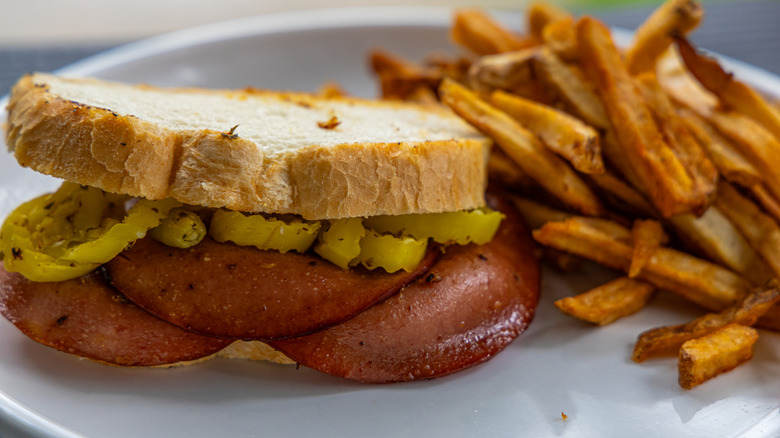 Fried bologna sandwich with peppers and fries on a white plate