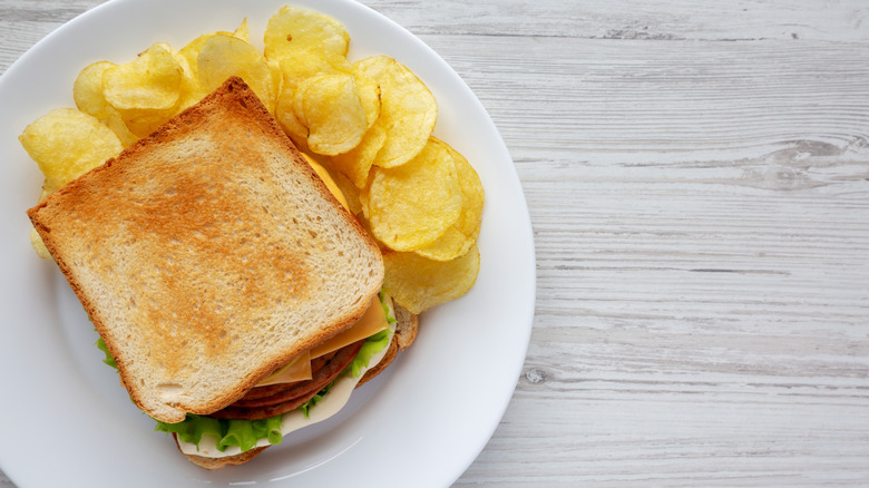 Bologna sandwich with chips on a white plate against a gray background