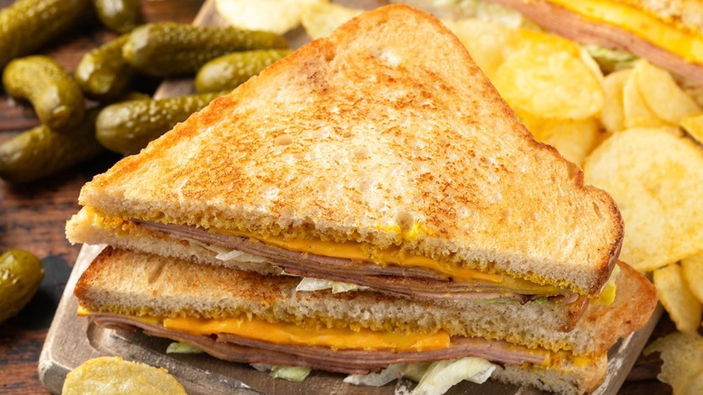 Fried bologna and cheese sandwich with a side of pickles on a wood surface