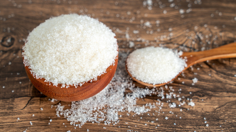 Granulated sugar in a wooden bowl and a wooden spoon on a rustic table
