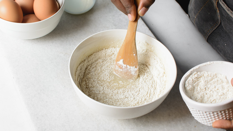 A person adding flour to a cake batter and mixing it