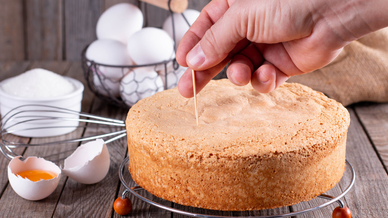 Person checking if a cake is ready with a toothpick