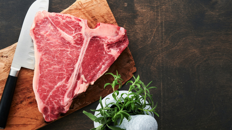 Thick cut raw T-bone steak on wooden cutting board