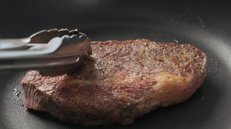 Steak being flipped with tongs