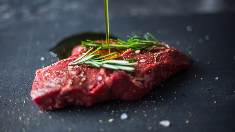 Raw steak being drizzled with oil