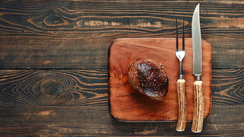 Steak resting on wooden cutting board ready to be cut