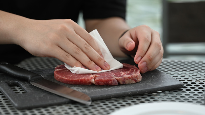 Two hands patting a steak dry with a paper towel