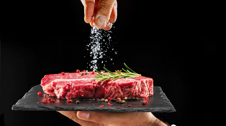 Chef sprinkling salt on raw ribeye steak
