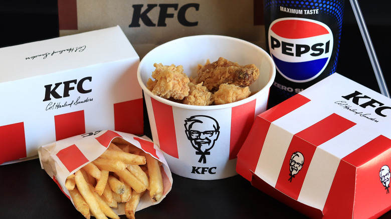 an assortment of KFC items, including fried chicken bucket, a Pepsi, biscuits, a sandwich, and french fries