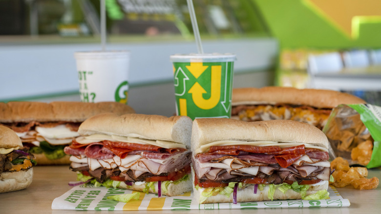 a group of Subway sandwiches together on a table with a heavily meat-stacked one front and center