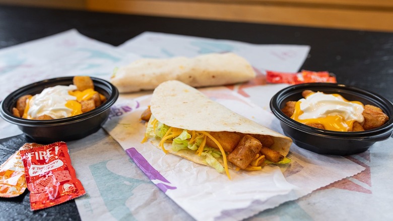 a Spicy Potato Soft Taco from Taco Bell lying on its wrapper between two orders of Cheesy Fiesta Potatoes from Taco Bell.
