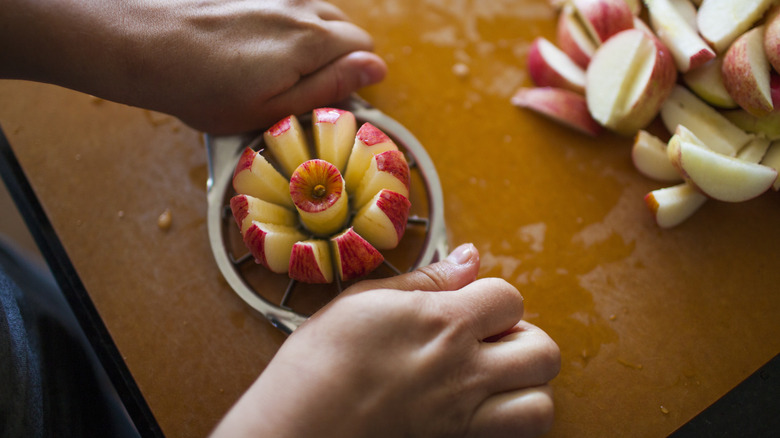 A person slices an apple using an apple slicer, with a pile of sliced apples next to it