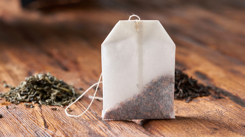 A tea bag, with piles of loose tea leaves next to it