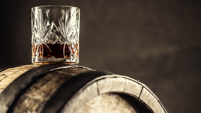 A glass of whiskey balances on an aging barrel