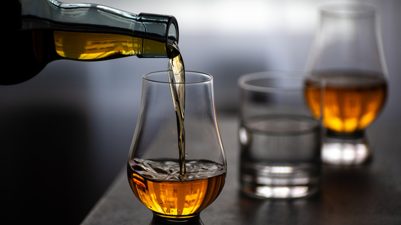 A person pours whiskey into a tulip glass