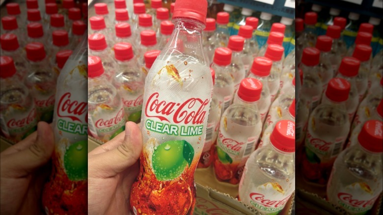 A bottle of Coca-Cola Clear Lime being held over a crate of Coca-Cola Clear Lime bottles.