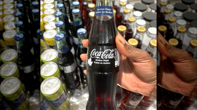 A glass bottle of Coca-Cola Quebec Maple being held over a row of soda bottles.